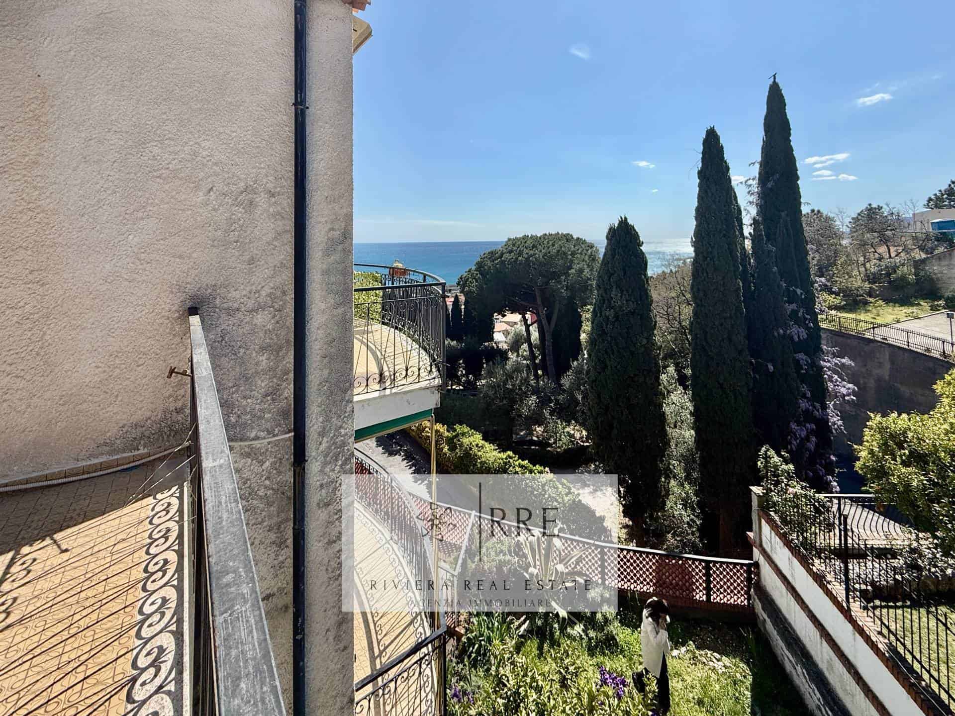 Seaside property with lush greenery, tall cypress trees, and ocean view in the background.