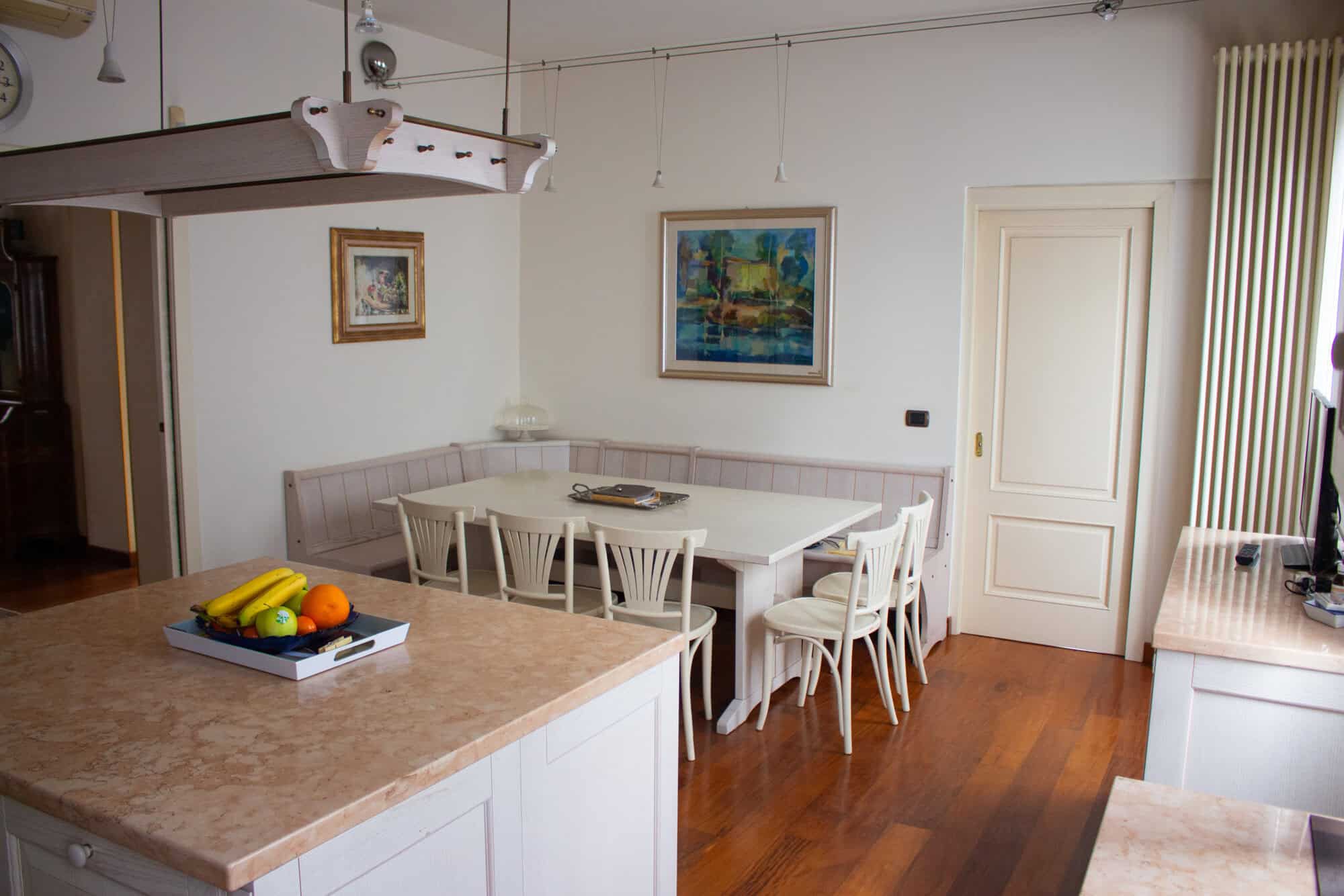 Bright dining room with white table and chairs, artwork on the wall, and wooden flooring.
