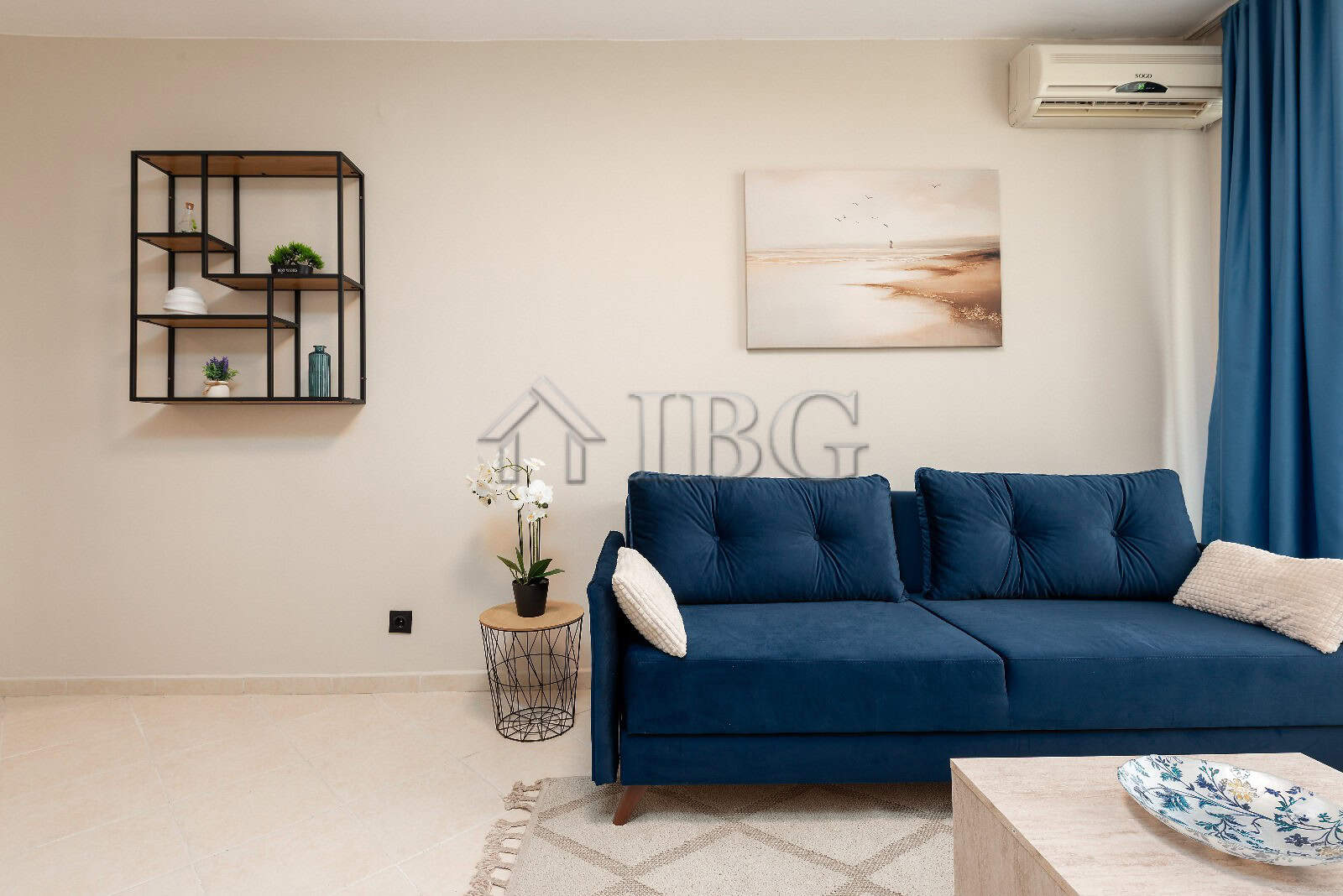 Modern living room featuring a blue sofa, wall art, and decorative shelves in a bright, airy space.
