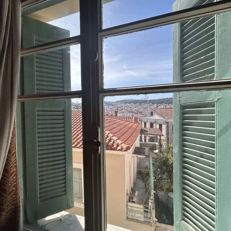 Open window with green shutters showing cityscape view.
