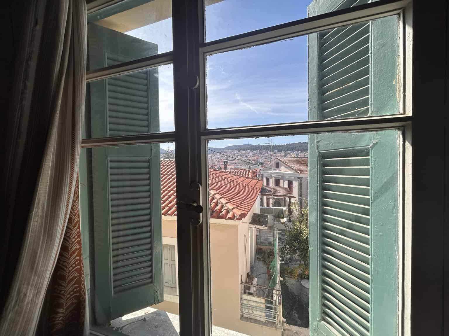 Open window with green shutters showing cityscape view.