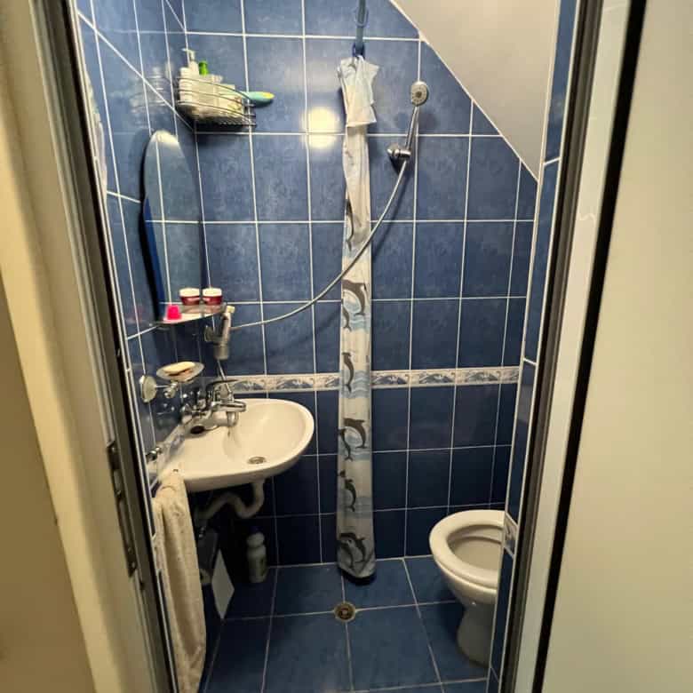 Small bathroom with blue tiles, shower, sink, and toilet in a maisonette.