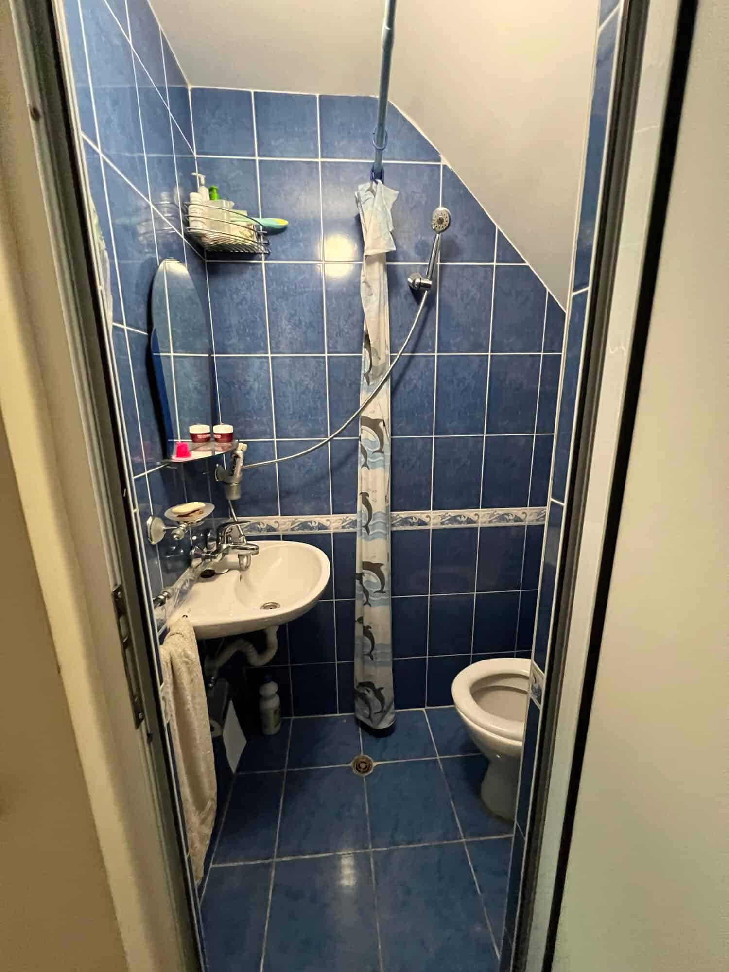 Small bathroom with blue tiles, shower, sink, and toilet in a maisonette.
