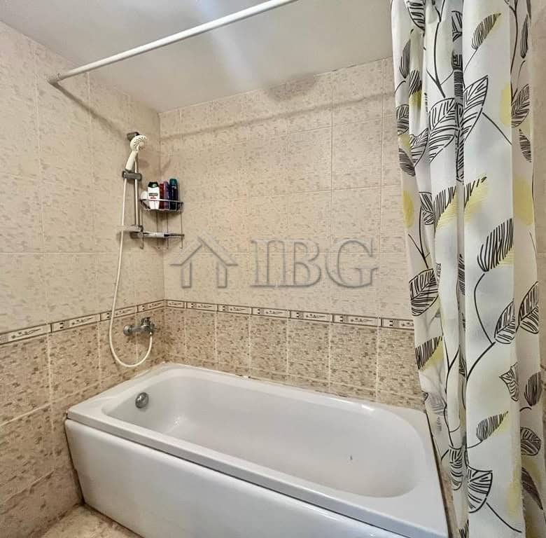 Bright bathroom featuring beige tiled walls, a bathtub, and a decorative shower curtain with leaf pa.