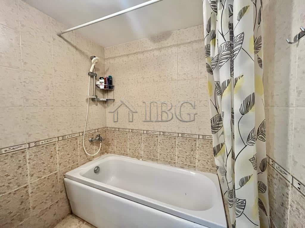 Bright bathroom featuring beige tiled walls, a bathtub, and a decorative shower curtain with leaf pa.