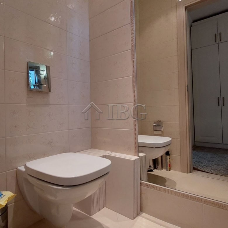 Bathroom with beige tiled walls, wall-mounted toilet, and a large mirror.