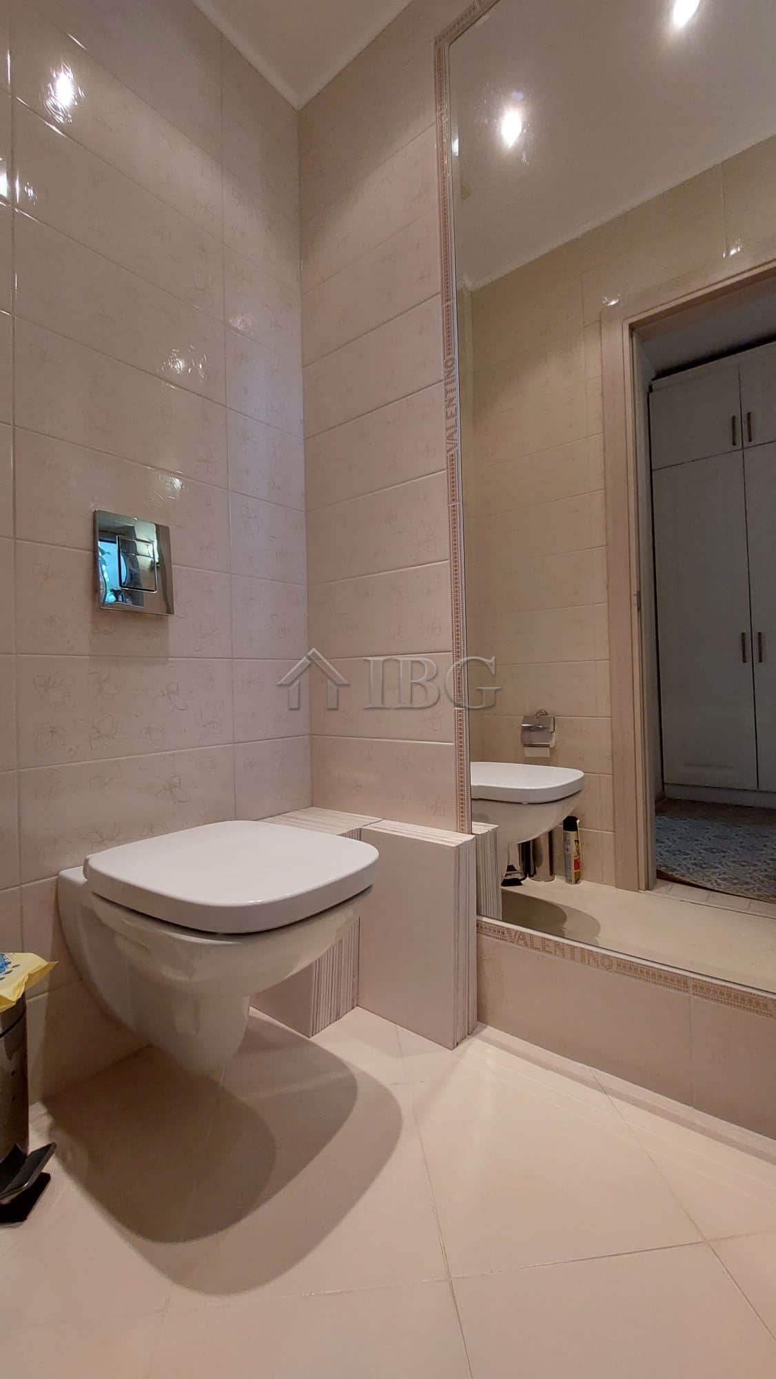Bathroom with beige tiled walls, wall-mounted toilet, and a large mirror.
