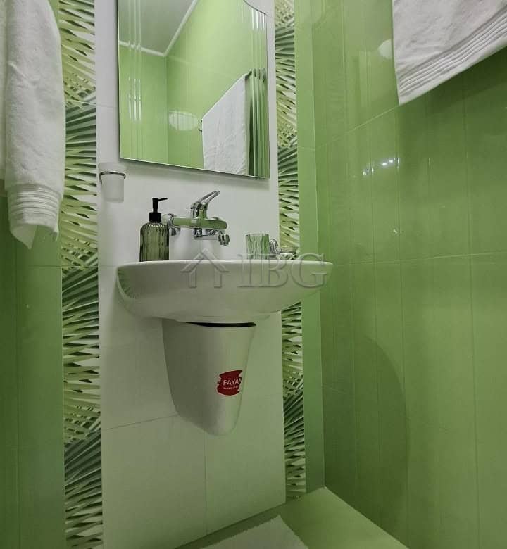 Bright green bathroom with compact sink, mirror, and towels in a spacious Nessebar apartment.