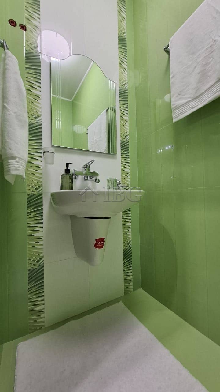 Bright green bathroom with compact sink, mirror, and towels in a spacious Nessebar apartment.
