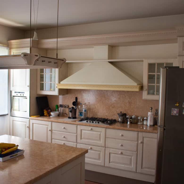 Modern white kitchen with beige countertops, stainless steel appliances, and ample natural light.
