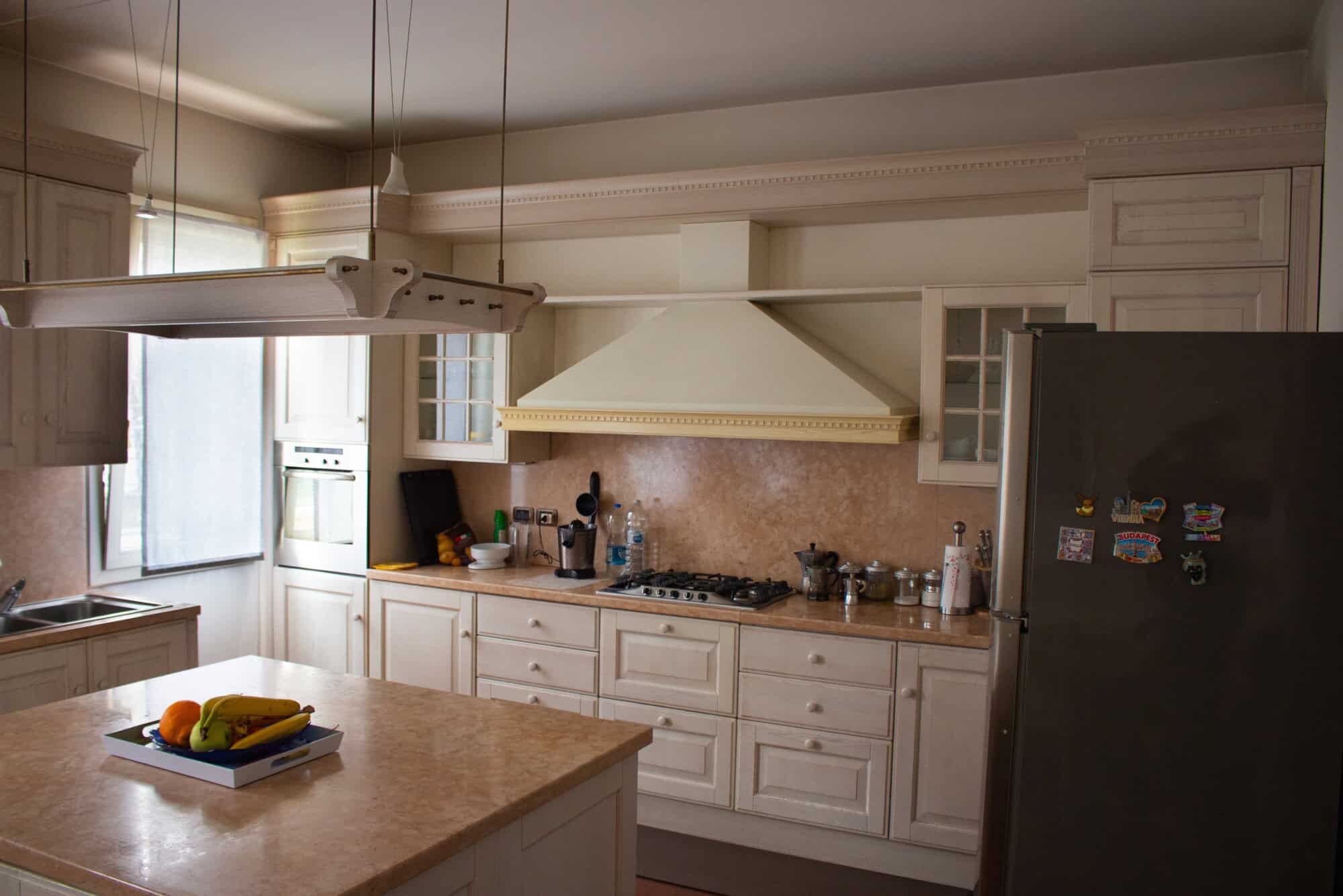 Modern white kitchen with beige countertops, stainless steel appliances, and ample natural light.