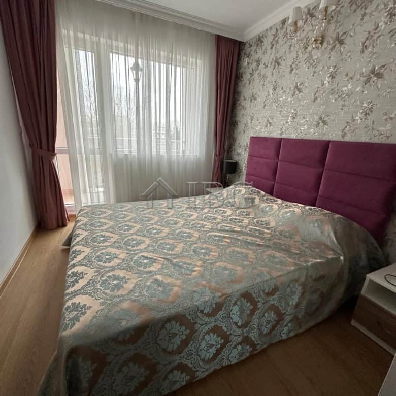 Cozy bedroom with a large window, elegant curtains, and a plush purple headboard. Bright, modern int.