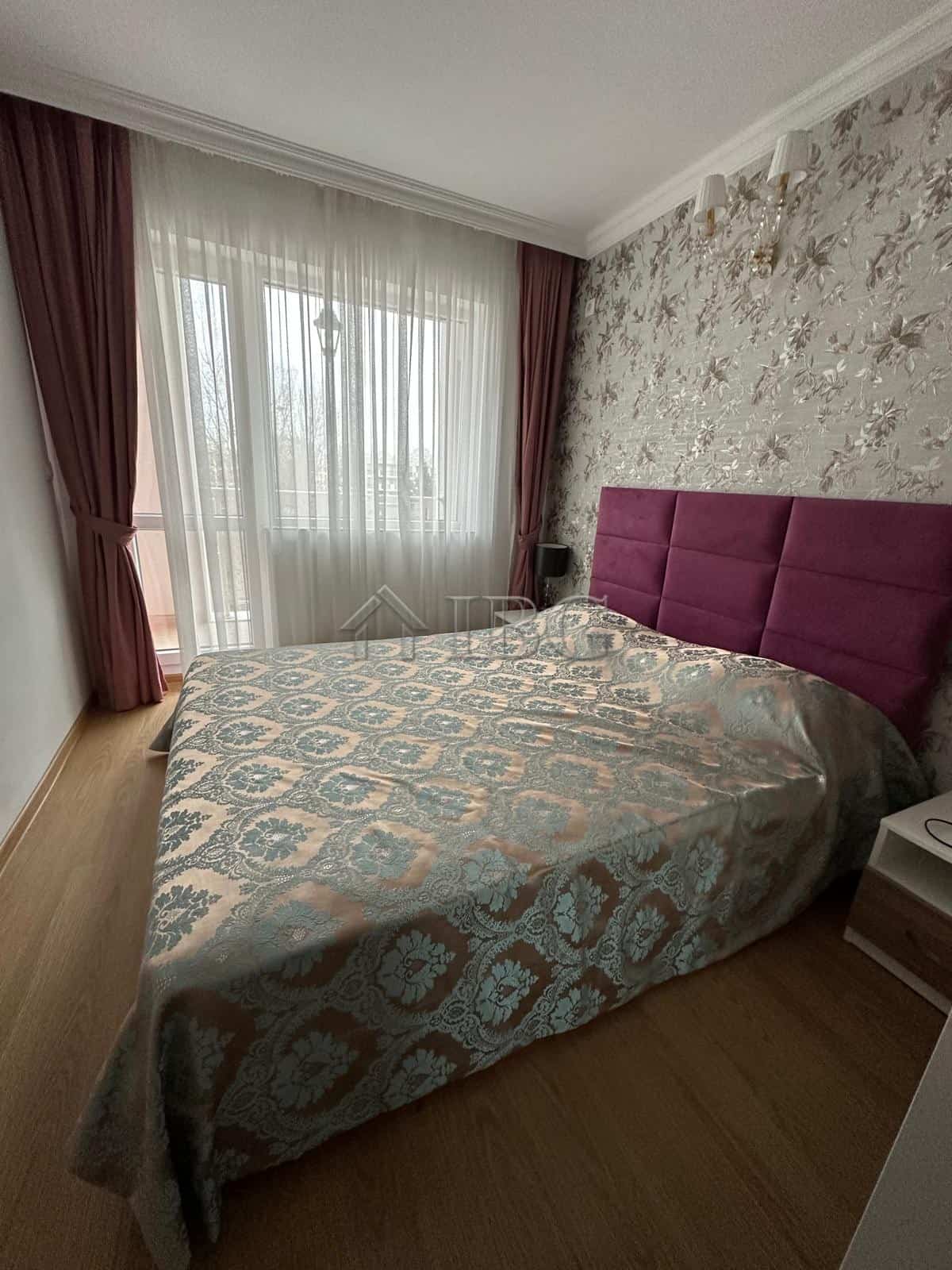 Cozy bedroom with a large window, elegant curtains, and a plush purple headboard. Bright, modern int.