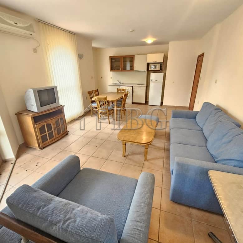 Bright living room with blue sofas, TV, and dining area overlooking the pool in Sunny Beach.