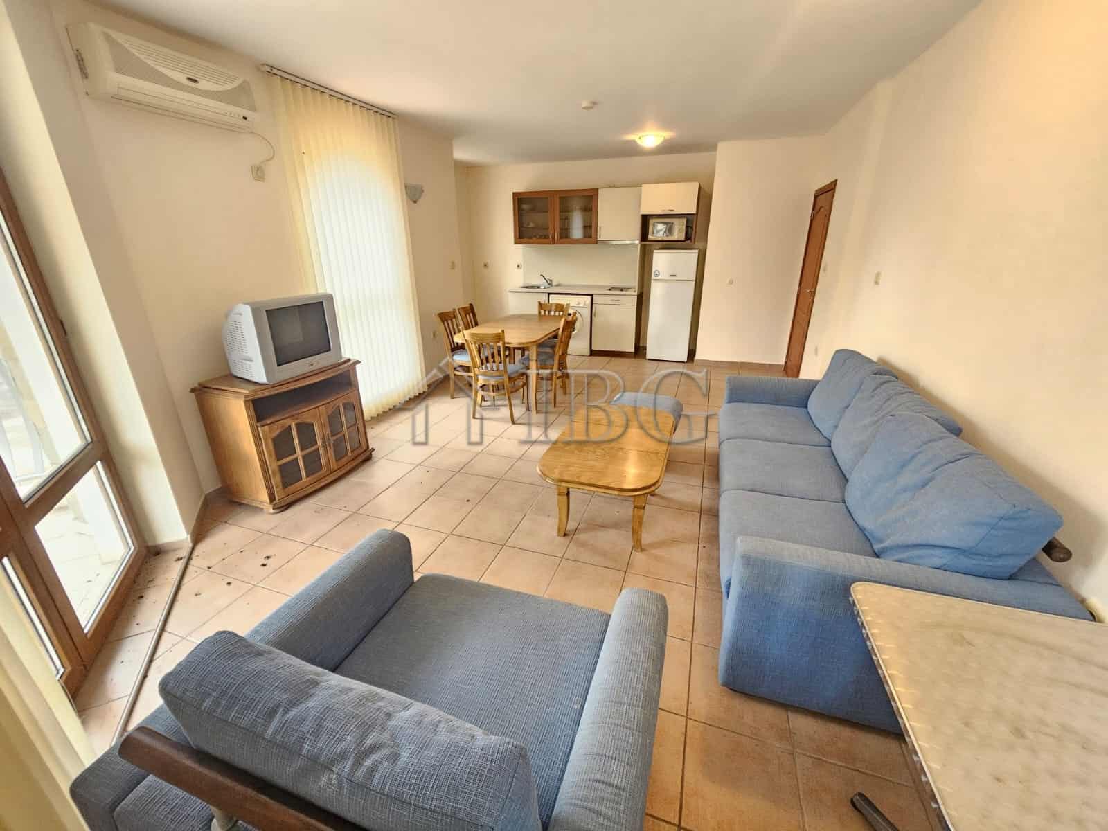 Bright living room with blue sofas, TV, and dining area overlooking the pool in Sunny Beach.