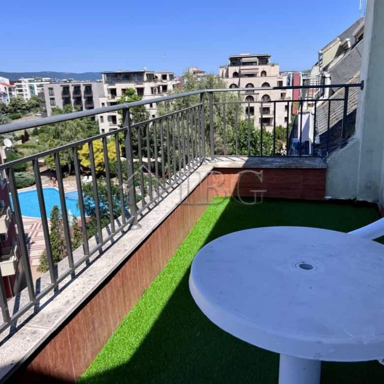 Balcony with pool view in Sveti Vlas apartment, featuring a small table and plastic chair.