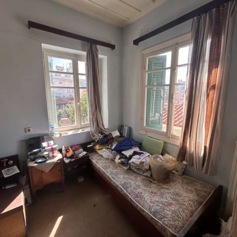 Bright bedroom with large windows and cityscape view, filled with natural light and personal belongi.