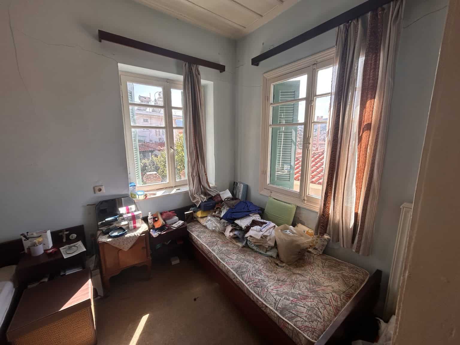 Bright bedroom with large windows and cityscape view, filled with natural light and personal belongi.