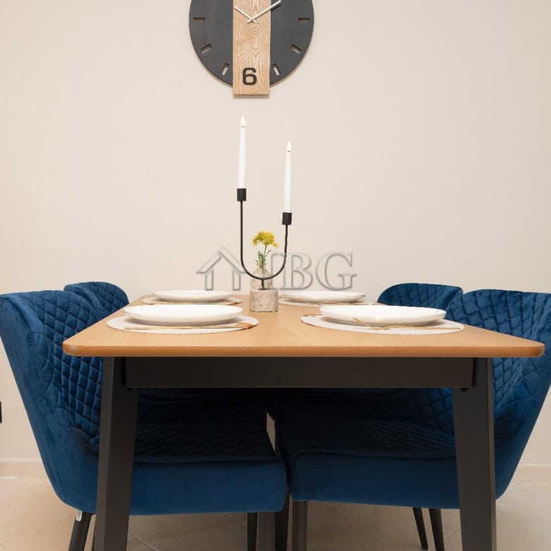Stylish dining table set with blue velvet chairs and minimalist wall clock.