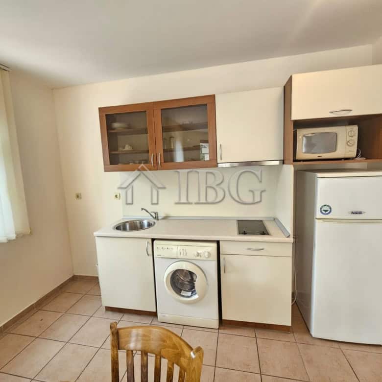 Bright kitchen with washing machine, fridge, and microwave in a sunny beach apartment.