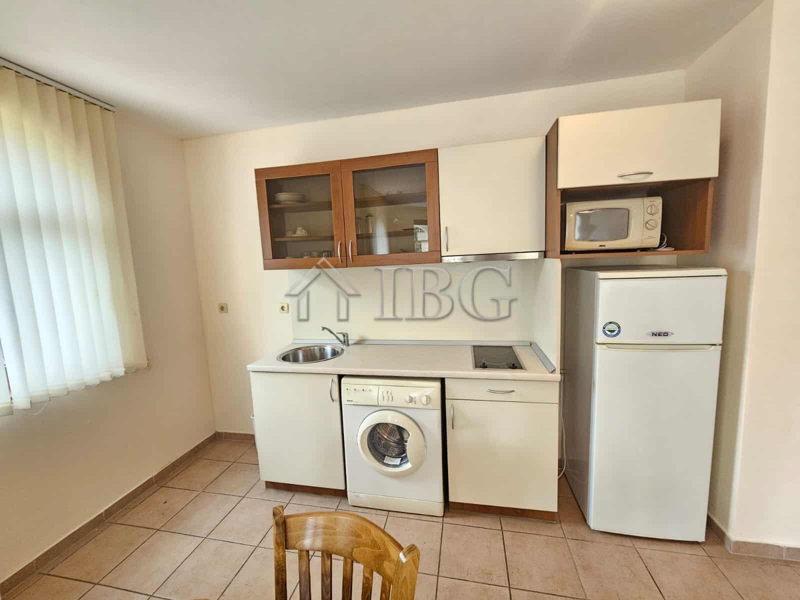 Bright kitchen with washing machine, fridge, and microwave in a sunny beach apartment.