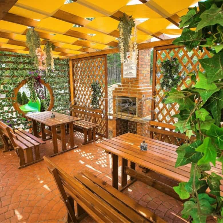 Outdoor patio with brick fireplace, wooden table, and lush greenery in Sunny Beach.