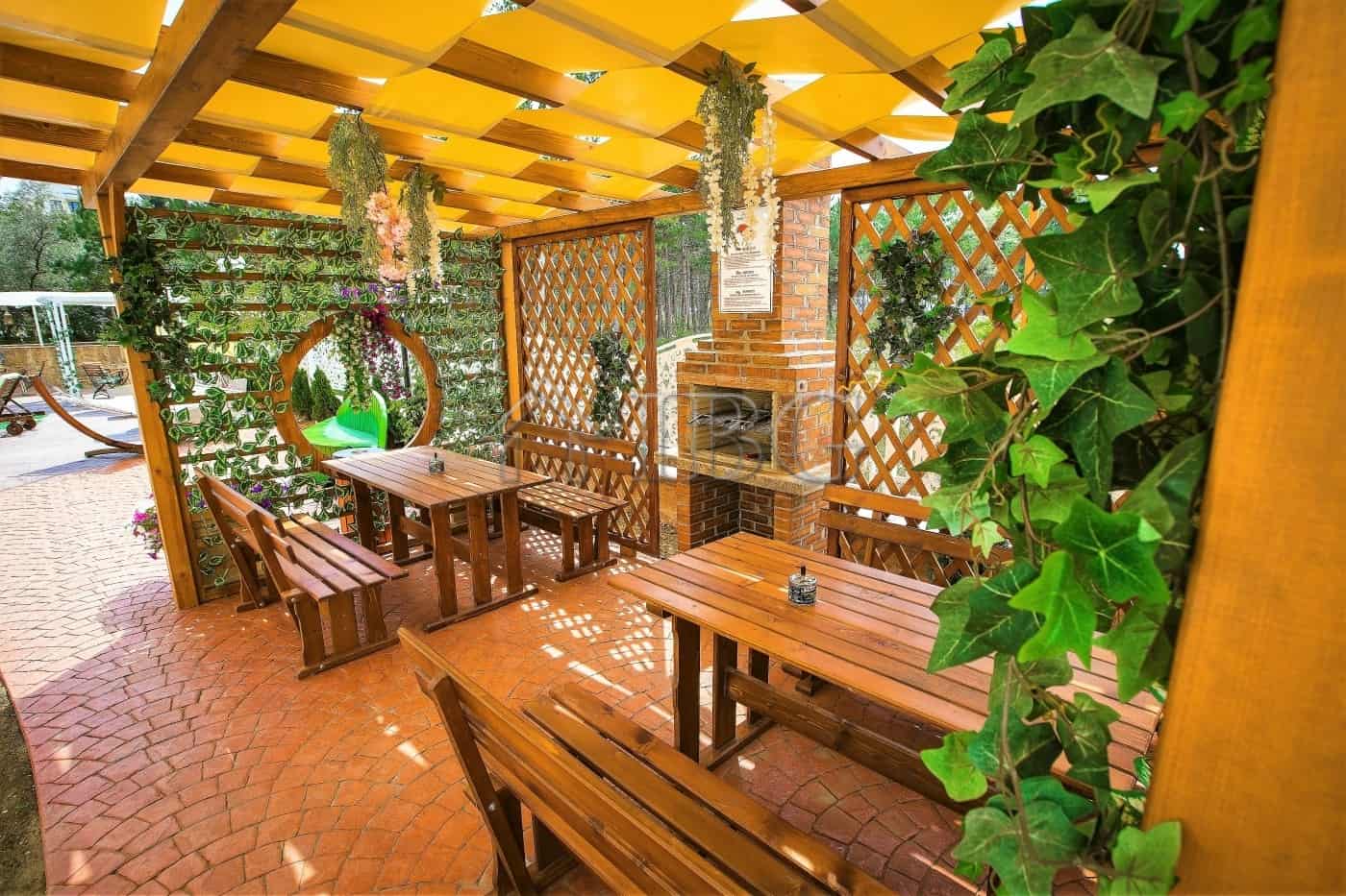 Outdoor patio with brick fireplace, wooden table, and lush greenery in Sunny Beach.