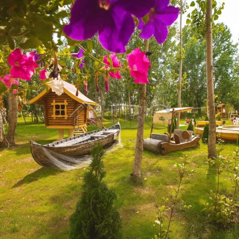 Charming outdoor scene with lush greenery, colorful flowers, and playful wooden boat and golf cart i.
