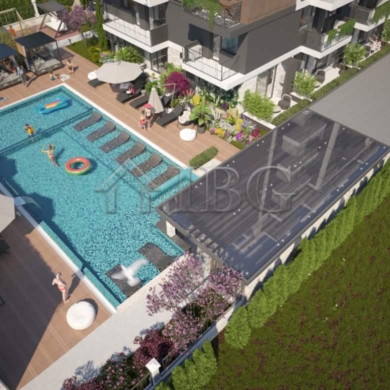 View of a modern apartment complex with a swimming pool and sun loungers in Sunny Beach.