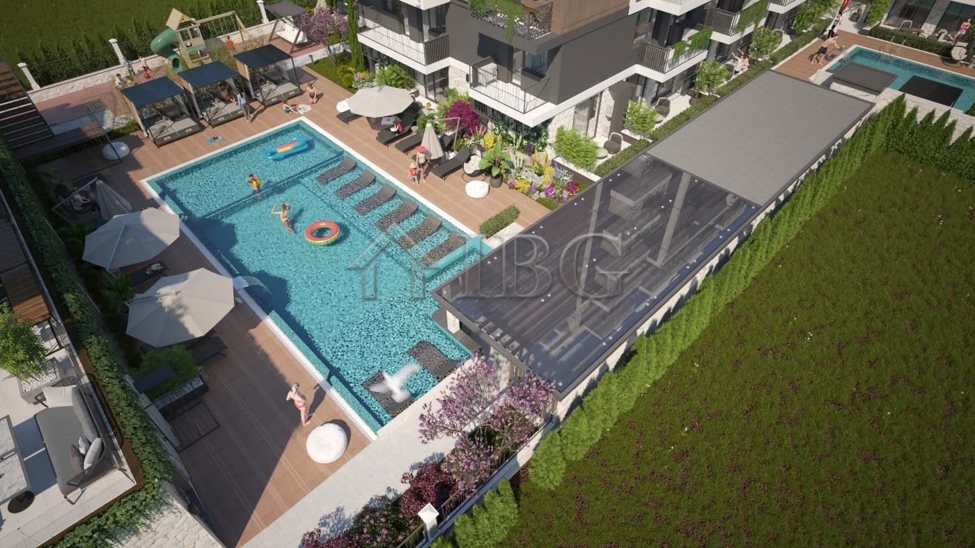 View of a modern apartment complex with a swimming pool and sun loungers in Sunny Beach.
