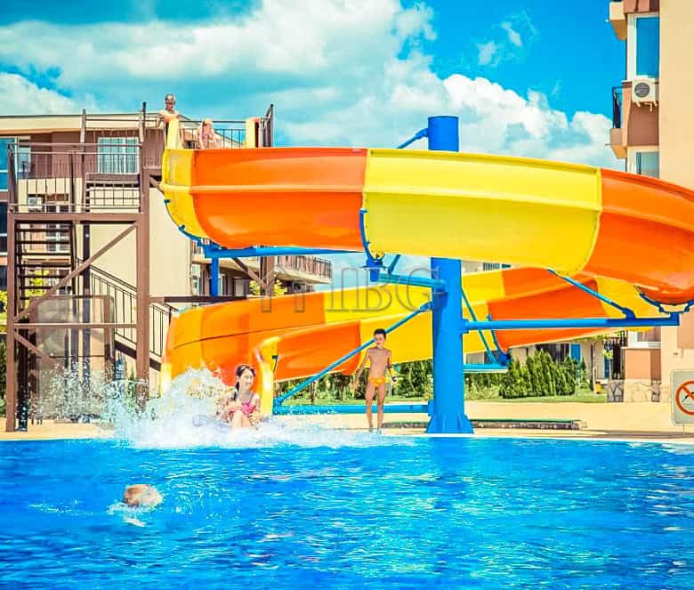 Pool with water slide and children enjoying the sunny day.