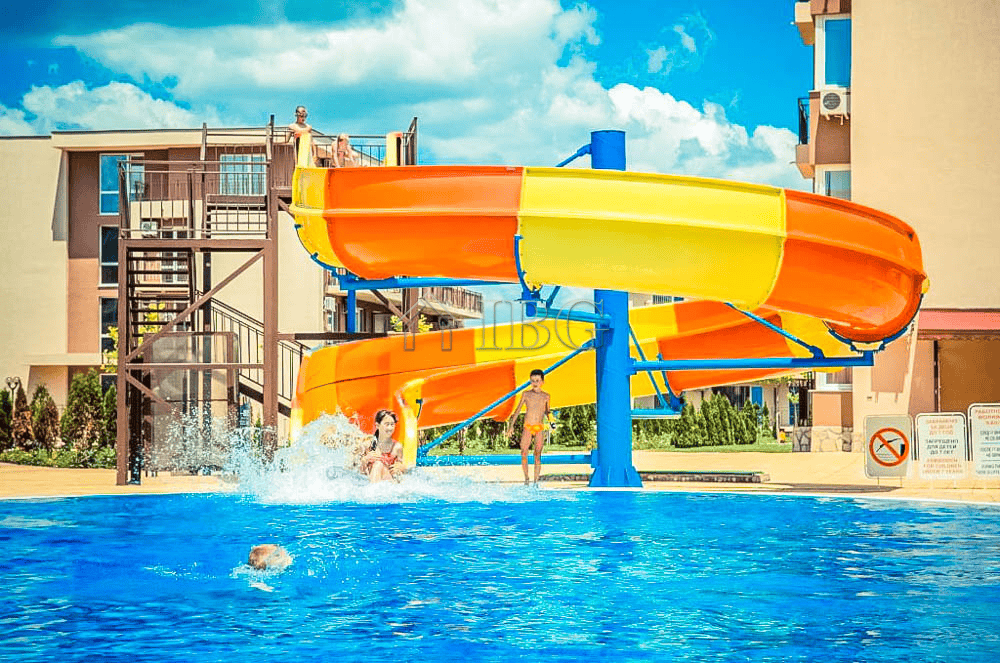 Pool with water slide and children enjoying the sunny day.