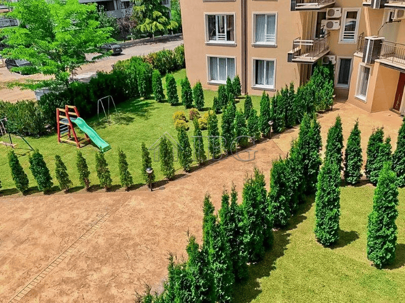 Bright apartment with balcony overlooking lush greenery and outdoor play space.