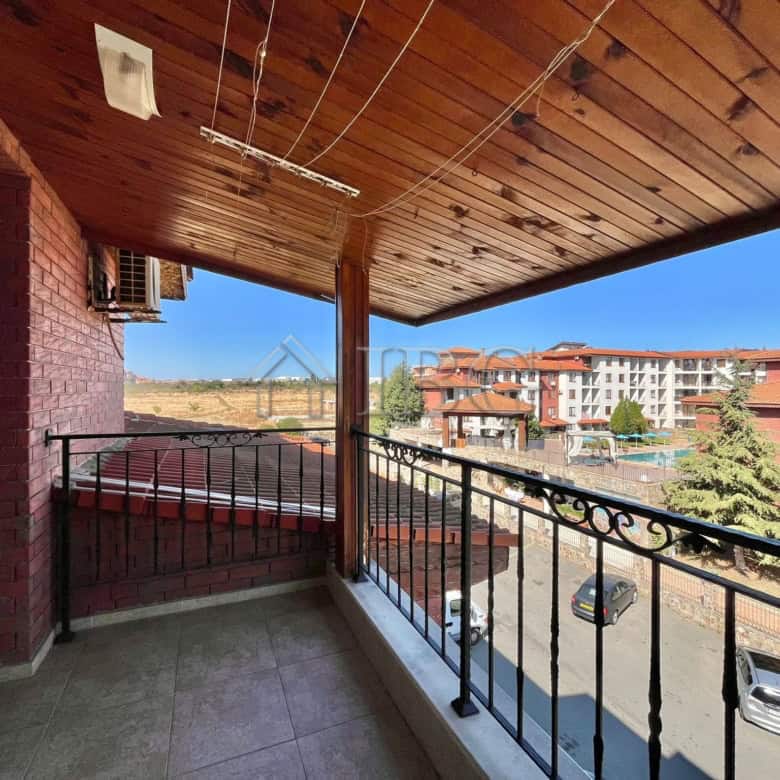 Balcony view of Ravda with a clear blue sky, overlooking nearby buildings and parking area.