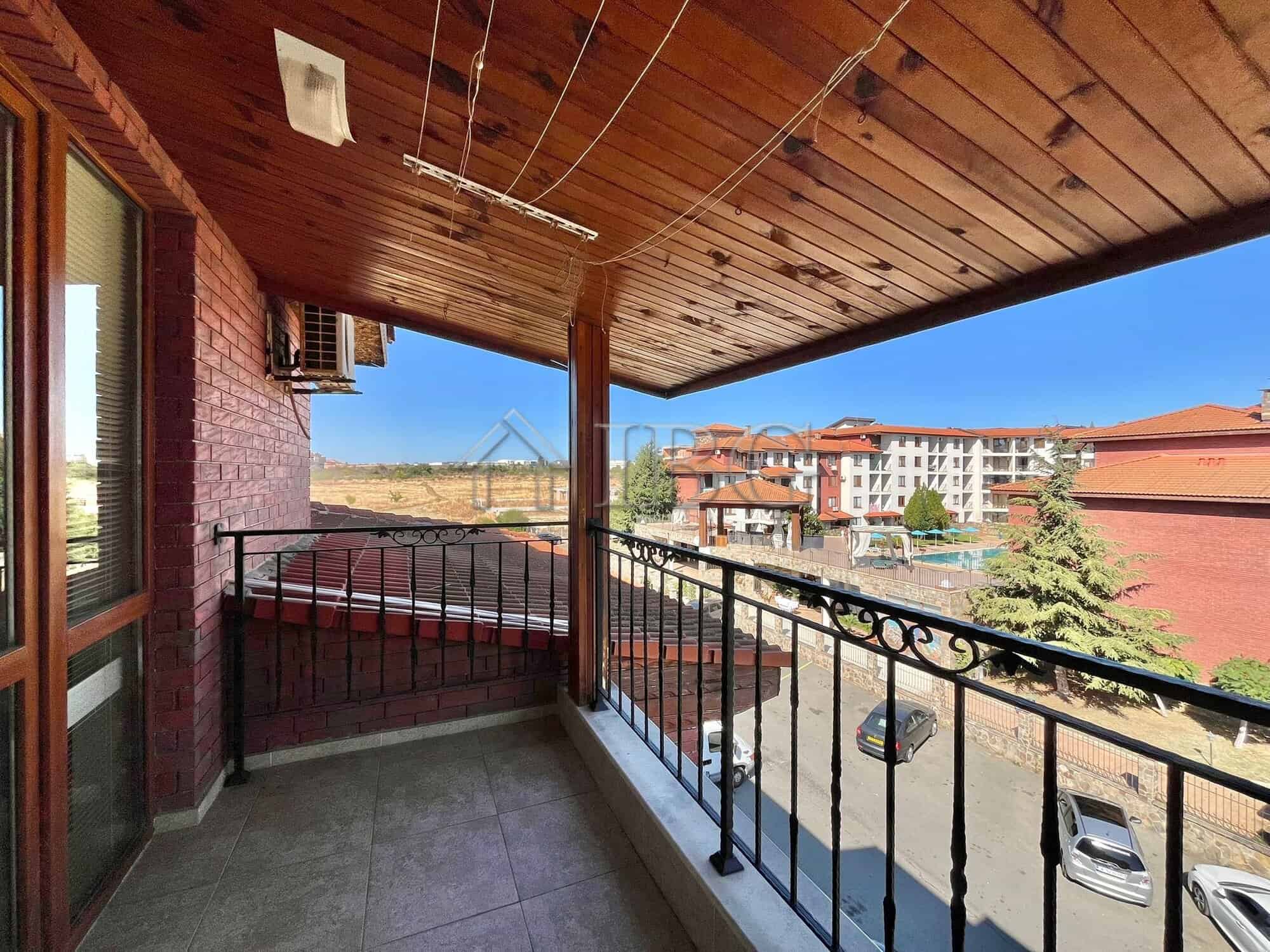 Balcony view of Ravda with a clear blue sky, overlooking nearby buildings and parking area.