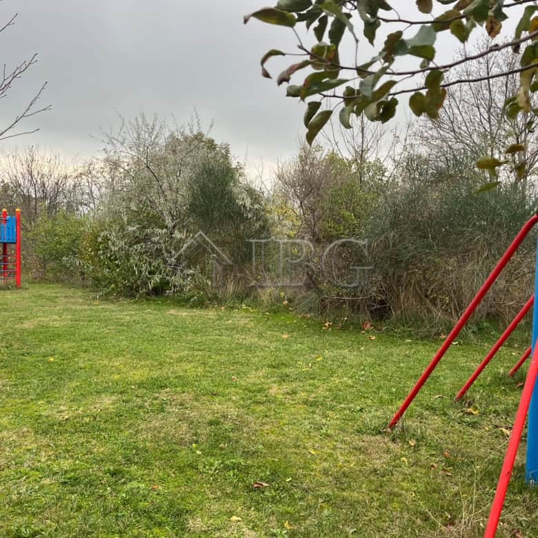 Bright outdoor scene showing a children's playground with slide and swings in a lush green garden se.