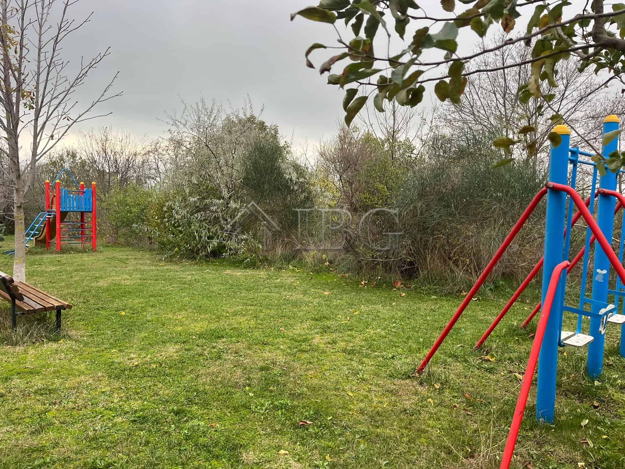 Bright outdoor scene showing a children's playground with slide and swings in a lush green garden se.