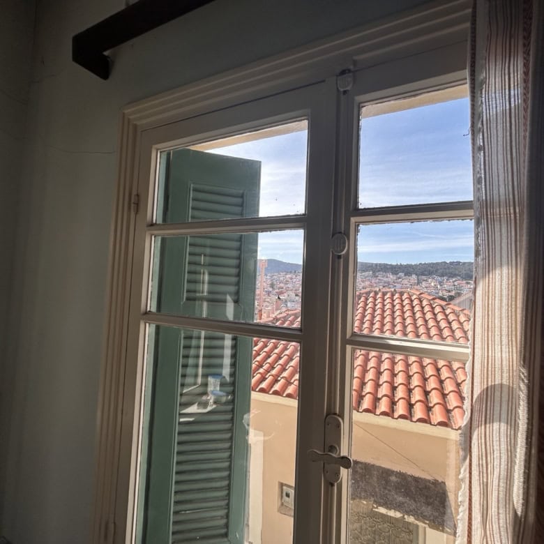 Cozy interior with a view of rooftops and the sea through a large window, showcasing Mediterranean a.