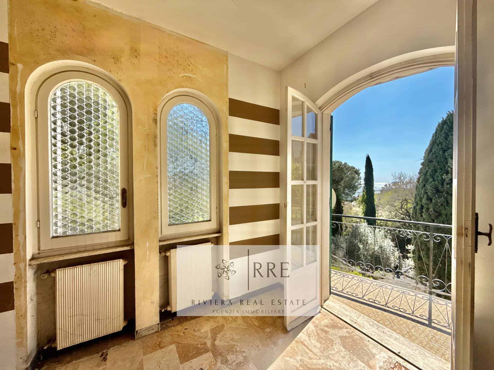 Balcony opening to lush garden with tall trees and clear blue sky.