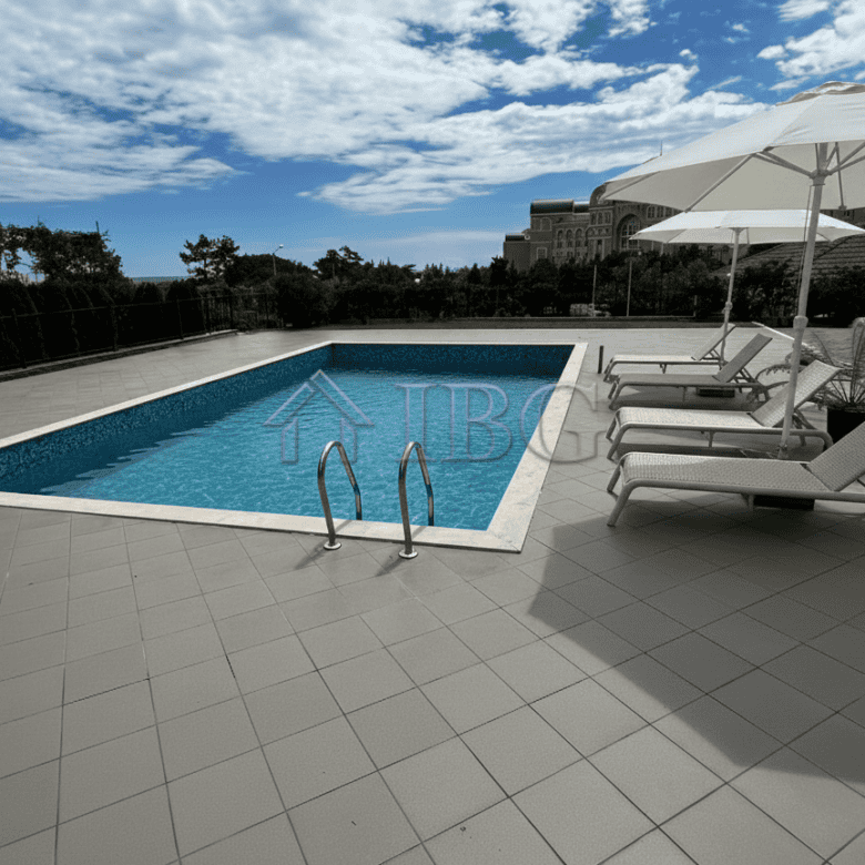 Pool with clear blue water, sun loungers, and umbrellas on a sunny day.