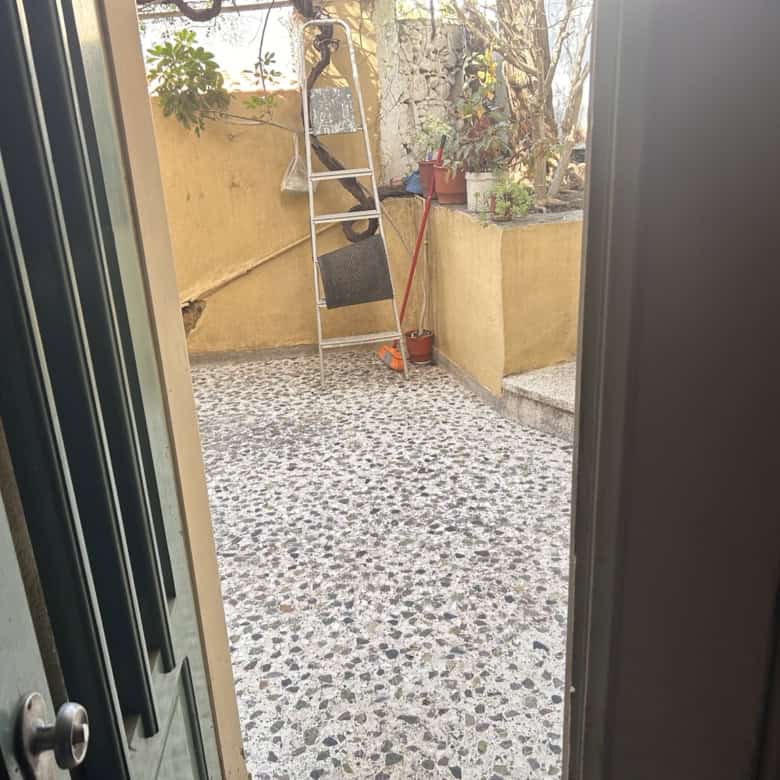 Outdoor patio with potted plants, ladder, and garden tools in a sunny backyard.