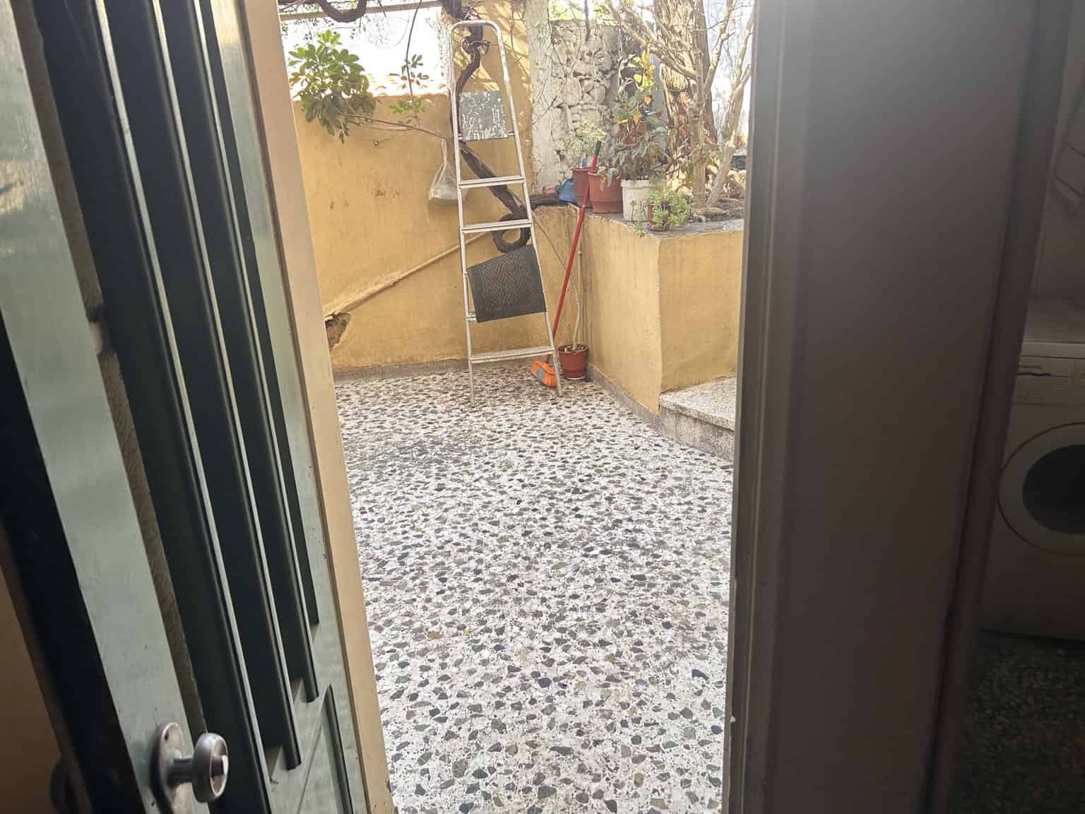 Outdoor patio with potted plants, ladder, and garden tools in a sunny backyard.