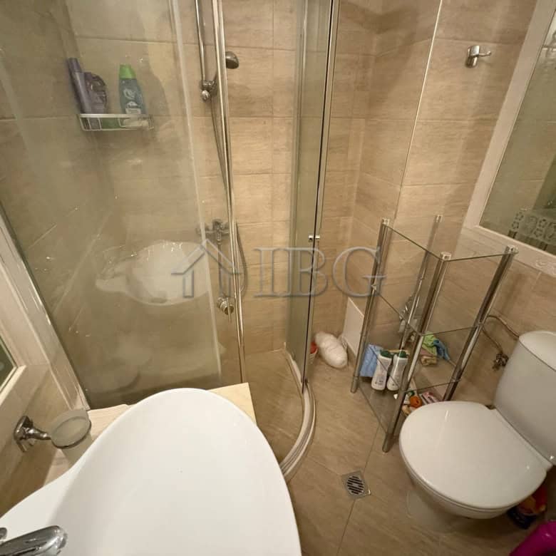 Bathroom with shower, toilet, and storage shelves in a sunny apartment.