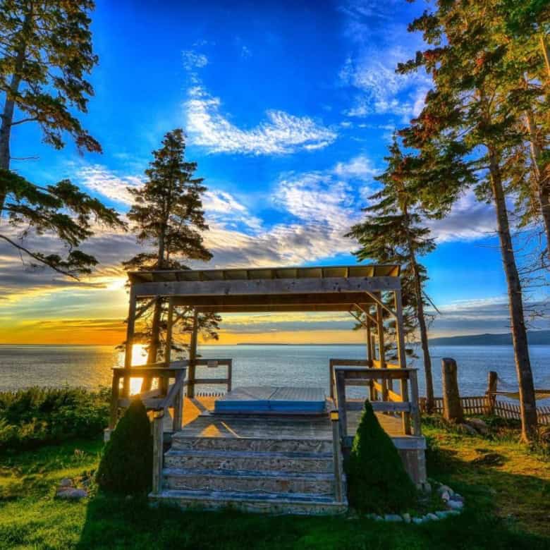 Ocean view porch at Sea Parrot Manor, Englishtown, Nova Scotia, with stunning sunset and coastal sce.