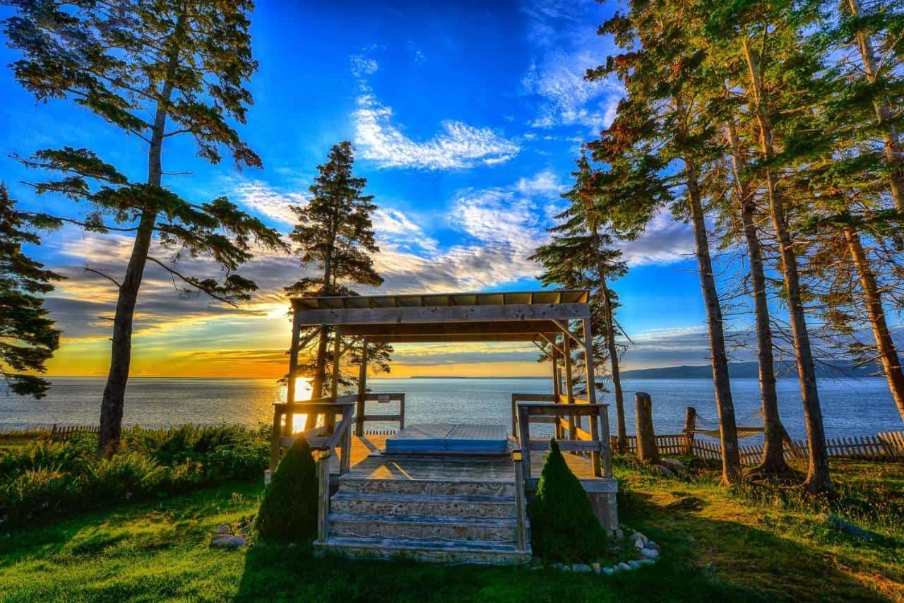 Ocean view porch at Sea Parrot Manor, Englishtown, Nova Scotia, with stunning sunset and coastal sce.