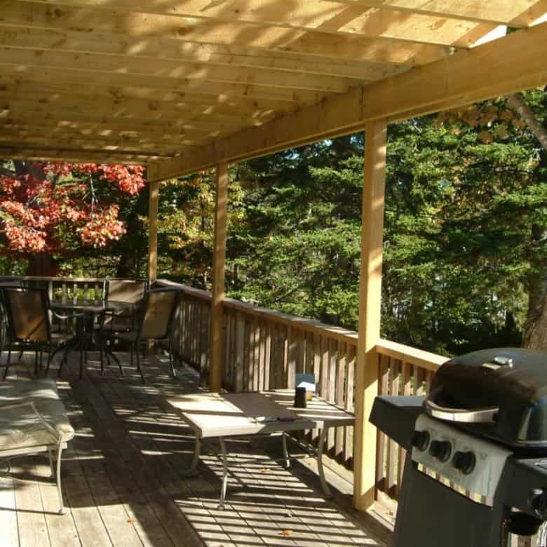Wooden deck with outdoor furniture and BBQ overlooking lush trees in Nova Scotia.
