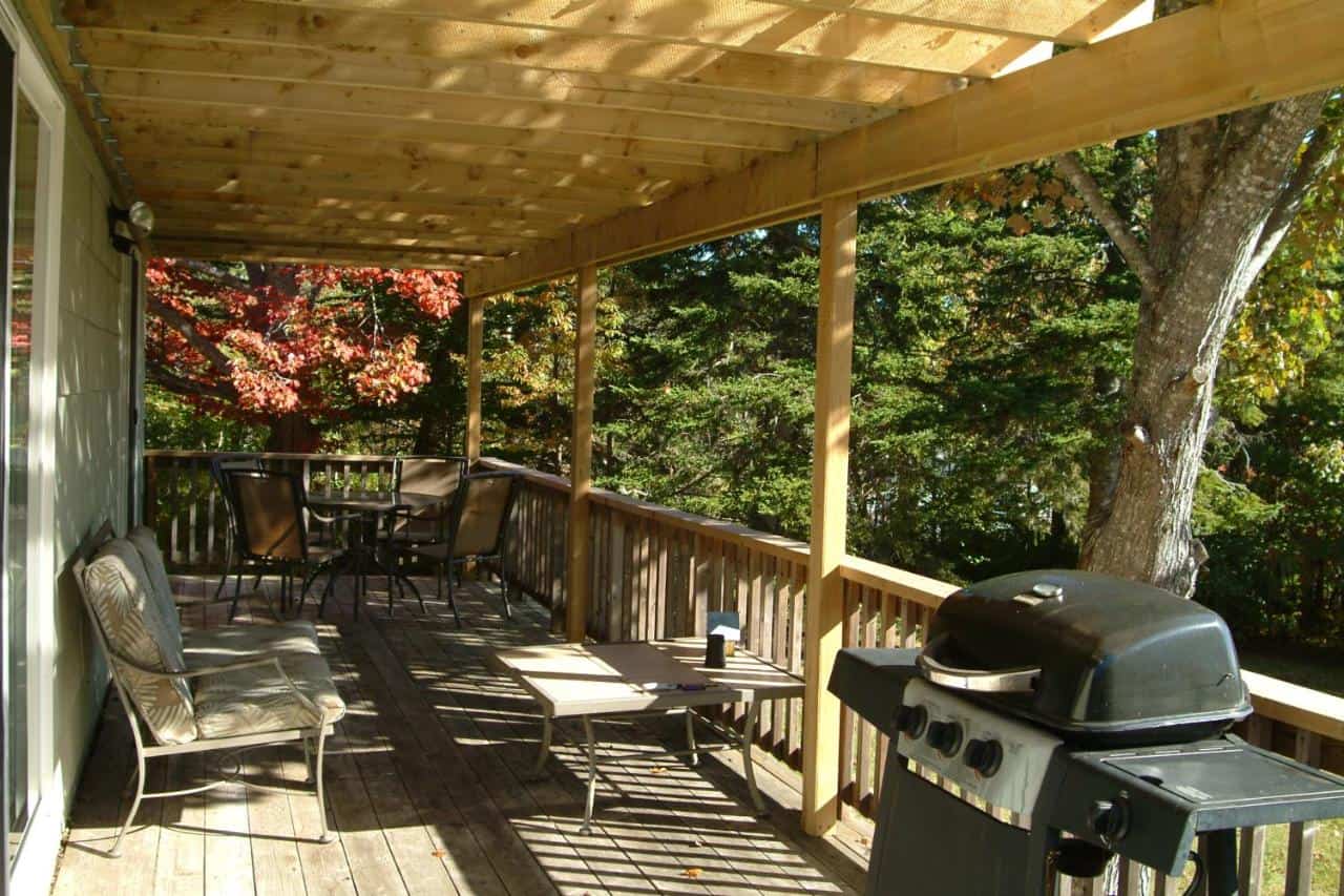 Wooden deck with outdoor furniture and BBQ overlooking lush trees in Nova Scotia.