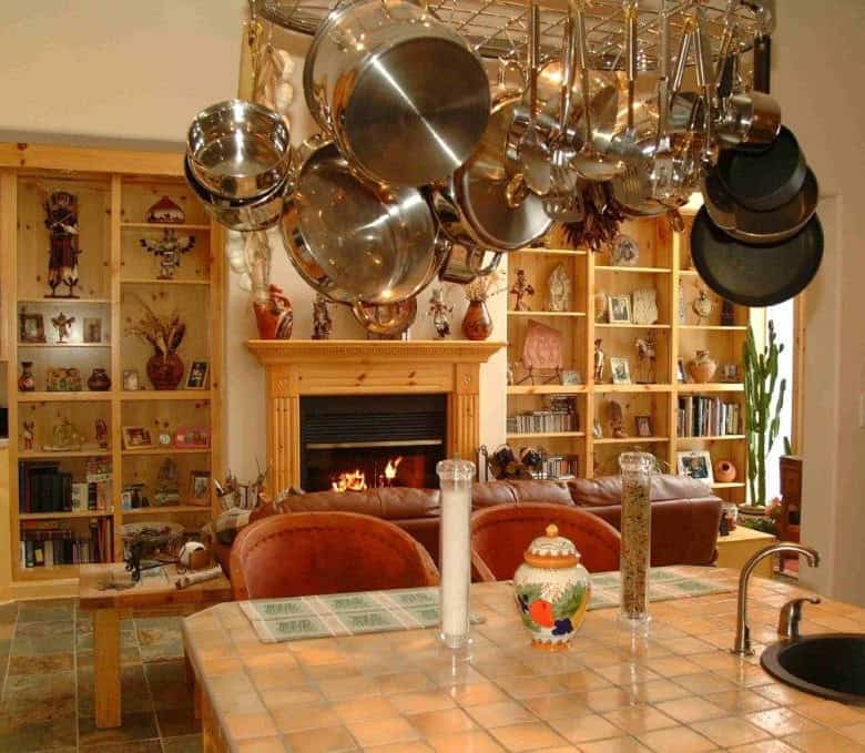 Interior view of a cozy kitchen with hanging pots and a warm fireplace in the background.