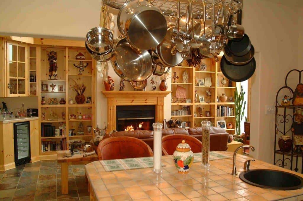 Interior view of a cozy kitchen with hanging pots and a warm fireplace in the background.