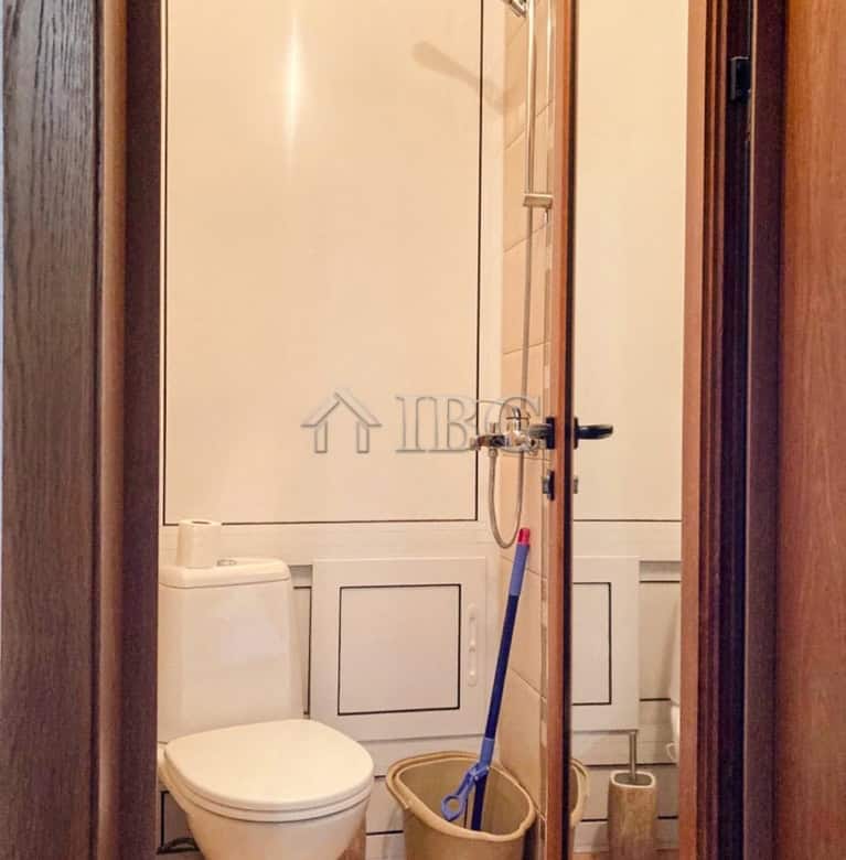 Small bathroom with toilet, shower, and cleaning tools in a Ruse apartment.